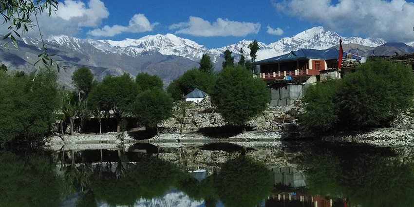 Nako Lake with perfect reflections of finely cut trees, buildings and snowy mountain peaks