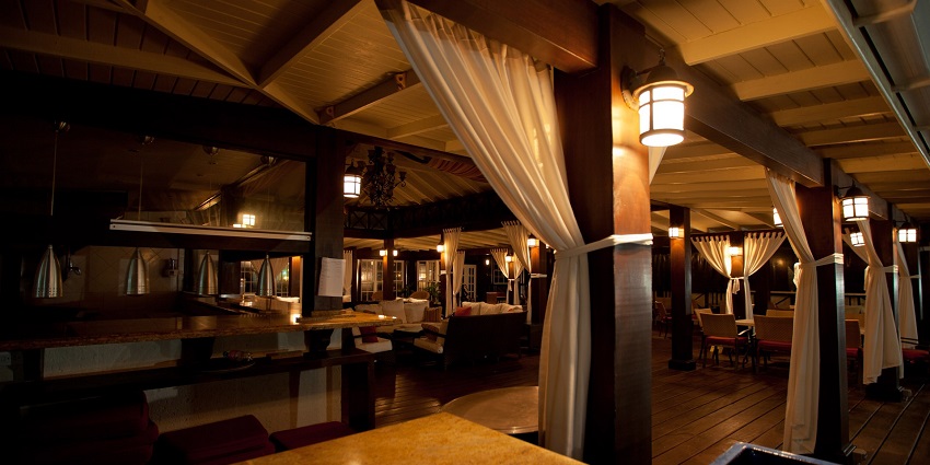 A warmly lit bar displays wooden beams, draped curtains, and cosy seating areas.