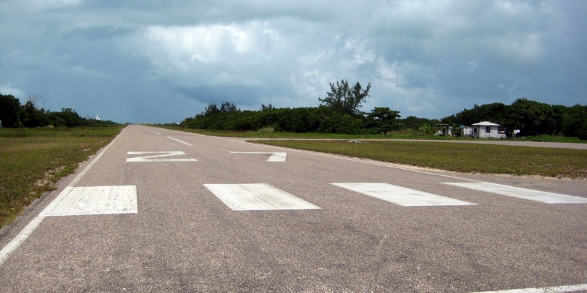 Long runway of Caye Caulker airport with markings on the runway surrounded by greenery