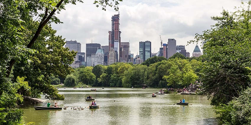 A lake at Central Park with under-construction skyscrapers of New York City in the background.