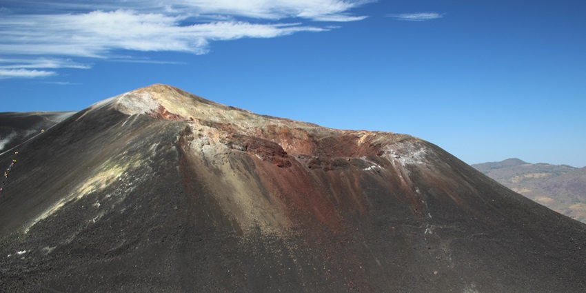 Cerro Negro volcano’s dark slopes rise against the sky, with a rugged volcanic landscape.