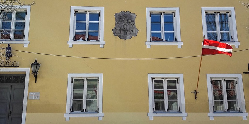 Capturing the Old Town Hall of Cēsis with its yellow facade and a Latvian flag waving.