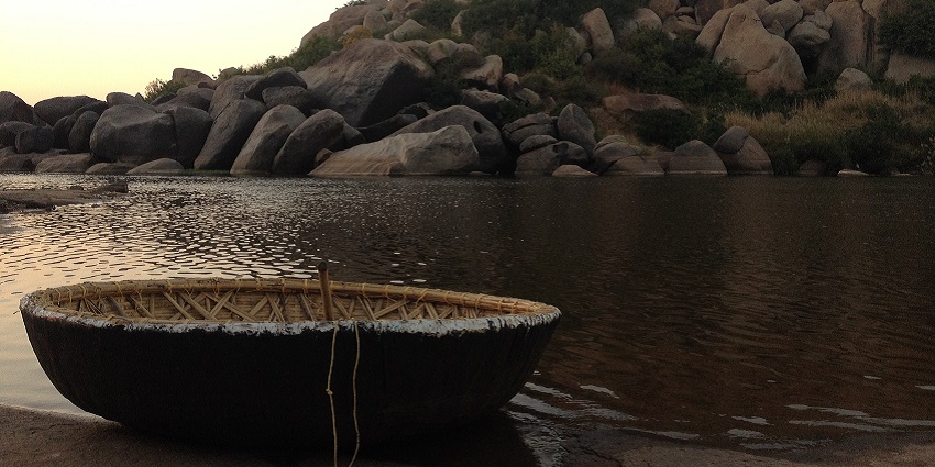 A peaceful coracle ride on a lake in Hampi, with reflections of boulders on water.