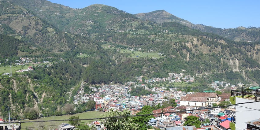 Scenic view of Chamba town nestled among mountains, lush trees, and colourful houses.