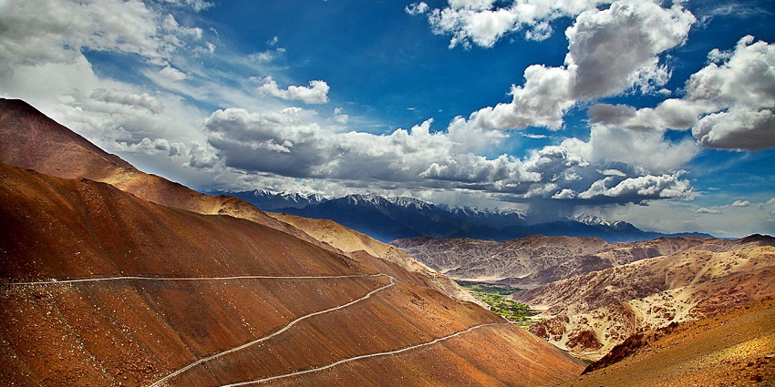 Chang La Pass with roads on sandy mountains and snowy mountain peaks under a clouded sky
