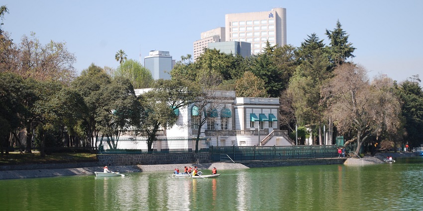People boating near the shores of Chapultepec Park with different buildings and greenery
