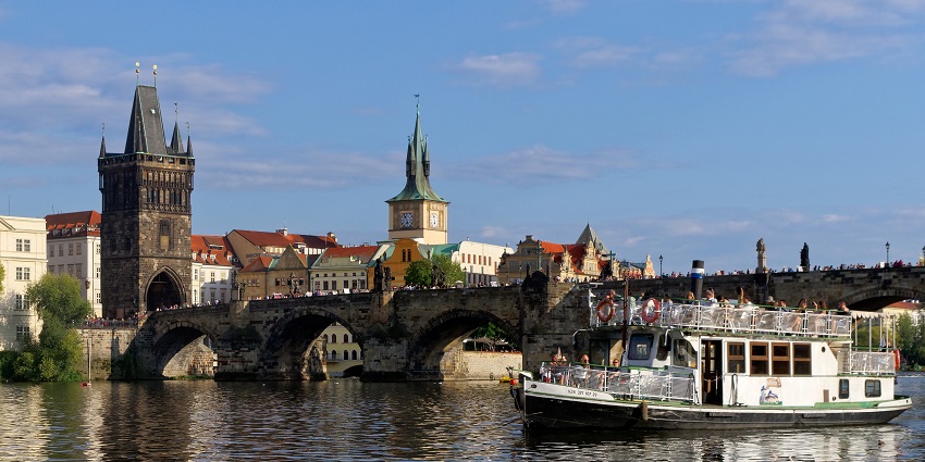 Charles Bridge is stretching over the Vltava, crowded with tourists and street artists