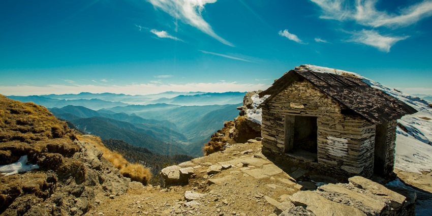 An image of a blue archway with bells, red flags, showcasing view of the starting point of the Chopta Chandrashila Trek, Uttarakhand.