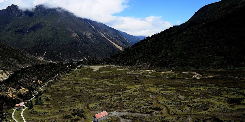 Chopta valley with small houses, red roofs, green plains and mountains covered in clouds