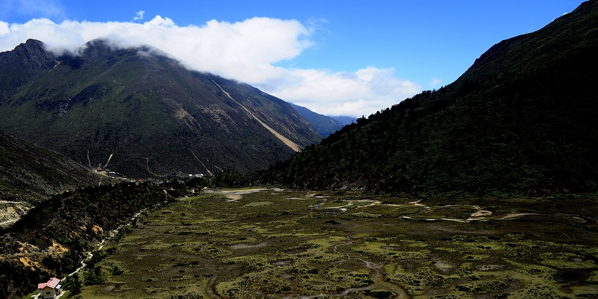 An aerial view of Chopta Valley surrounded by lush greenery and mountain ranges.