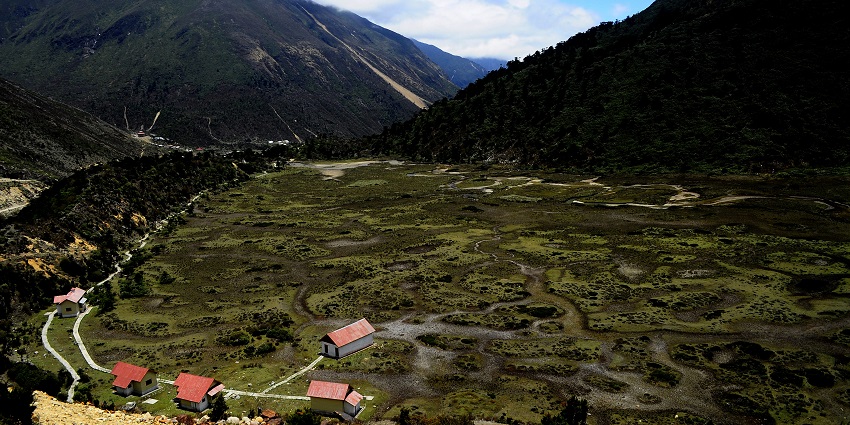 Chopta valley with small houses, red roofs, green plains and green mountains covered in clouds