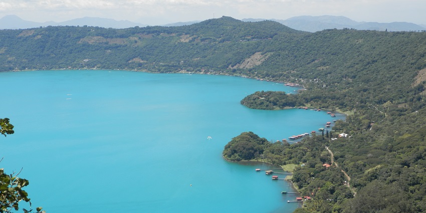 The turquoise waters of Lago de Coatepeque are stretching along the green shoreline.
