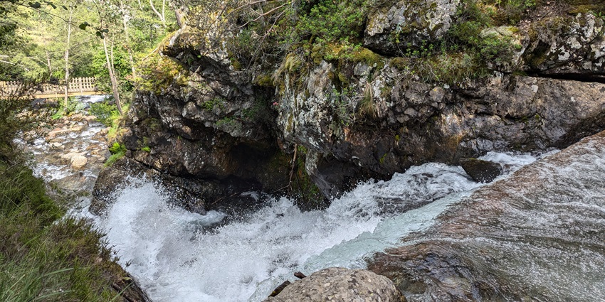 Water is flowing rapidly over rocks while surrounding trees are standing and swaying gently.
