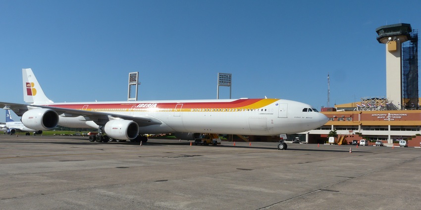 An airplane with red and yellow stripes parked at an airport near the clock tower building.