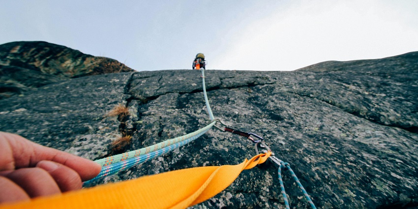 An image of a person rock climbing, gripping a yellow strap, secured with ropes, resembling rock climbing in Paro