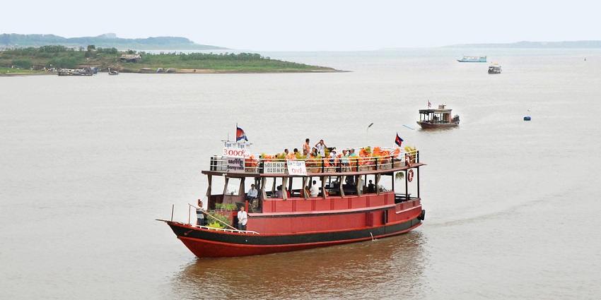 An image of a red passenger boat with flags, cruising through the Tonle Sap and Mekong waterways.