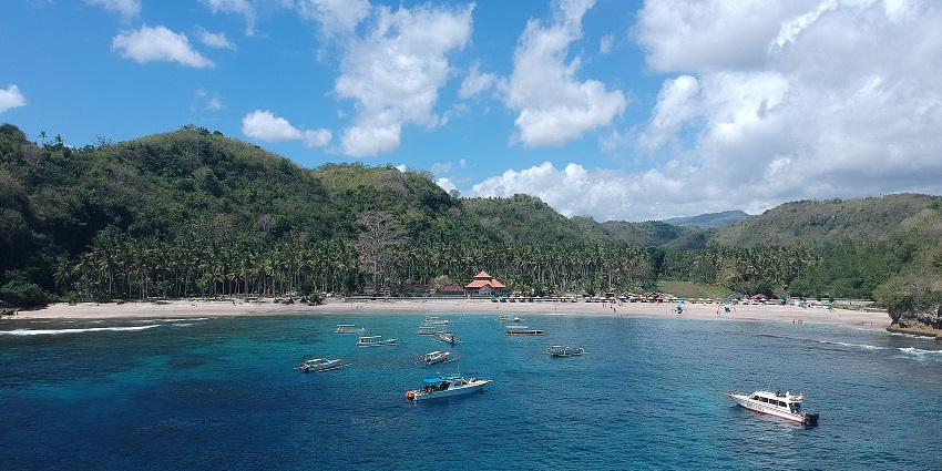 Crystal Bay in Nusa Penida with calm, clear blue waters surrounded by green hills and a quiet sandy beach.