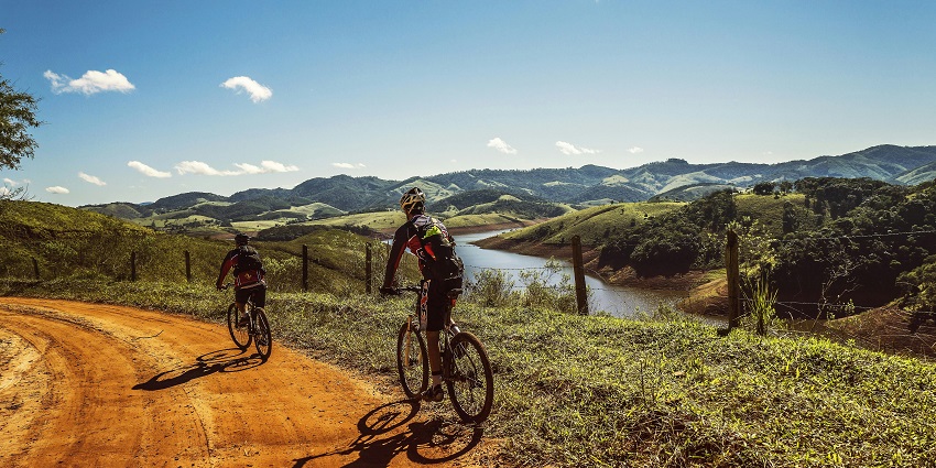 An image of two cyclists riding on a dirt road in hilly terrain, resembling the mountain biking experience in Paro