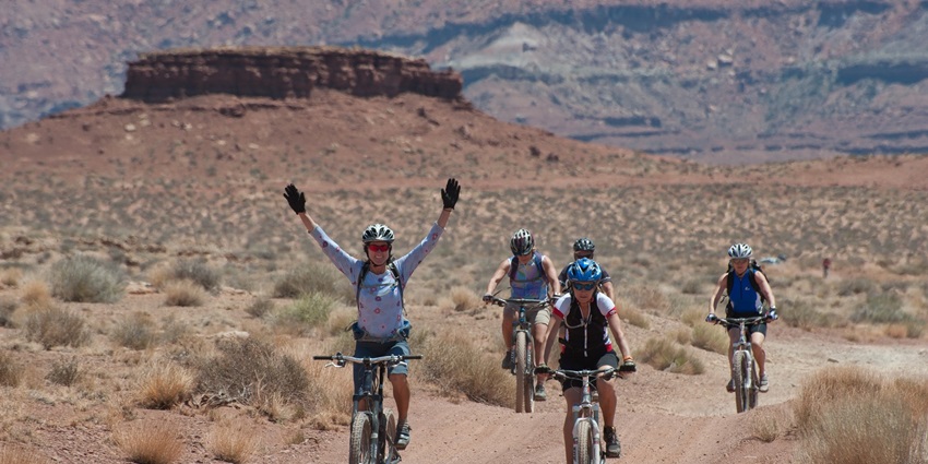 A group of cyclists is riding along a dusty desert trail, enjoying the scenic landscape.