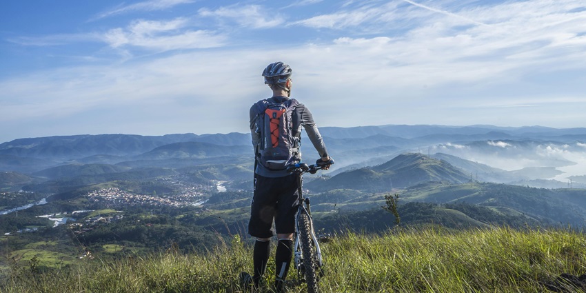 Image of a biker Holding Mountain Bike on Top of Mountain With Green Grass