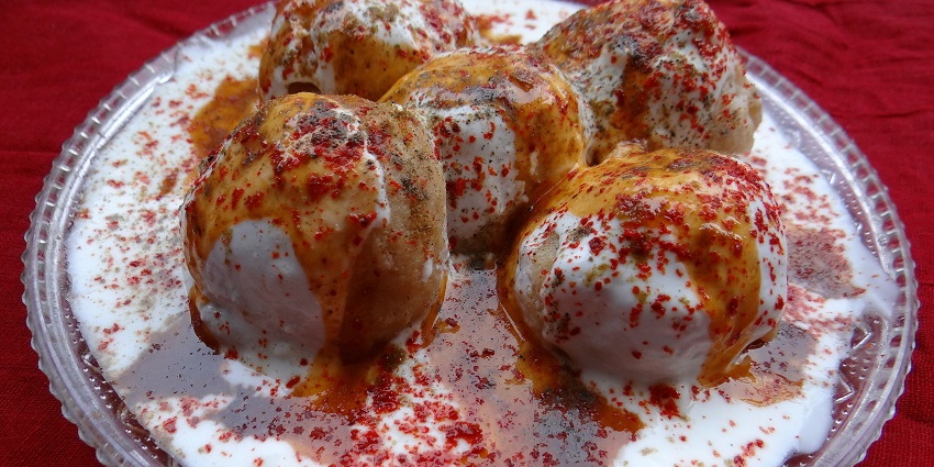 An image showing Dahi Vadas topped with yoghurt, chutneys, and spices on a serving plate.