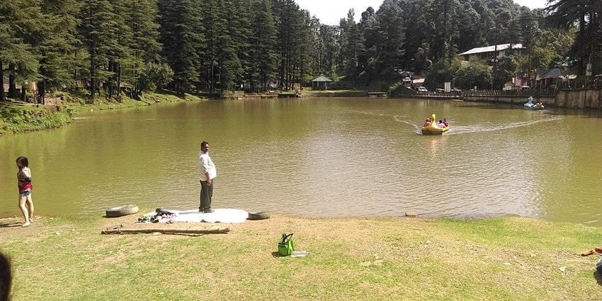 Serene lake reflecting surrounding trees and mountains with boats floating near the shore.