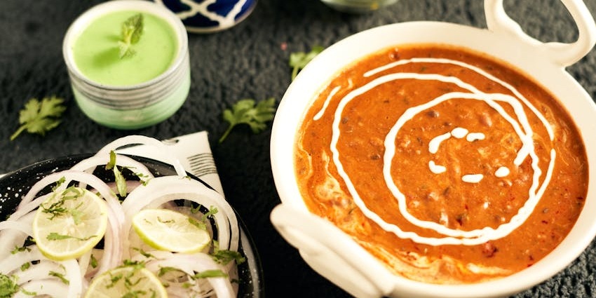 A plate of the tasty and creamy dal makhani in a bowl with butter and naan on the side