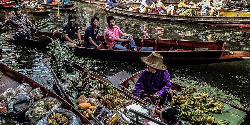 A floating market in Thailand with vendors selling goods from wooden long-tail boats.