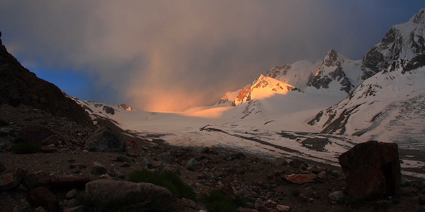 Darkot pass with a rocky surface, snowy mountains and clouds partially covering the hill
