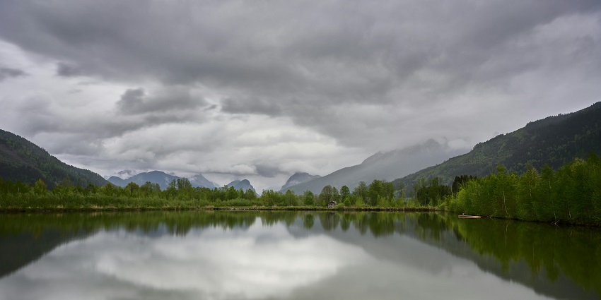 Misty lake rests beneath a dramatic cloudy evening sky, creating a moody and peaceful scene