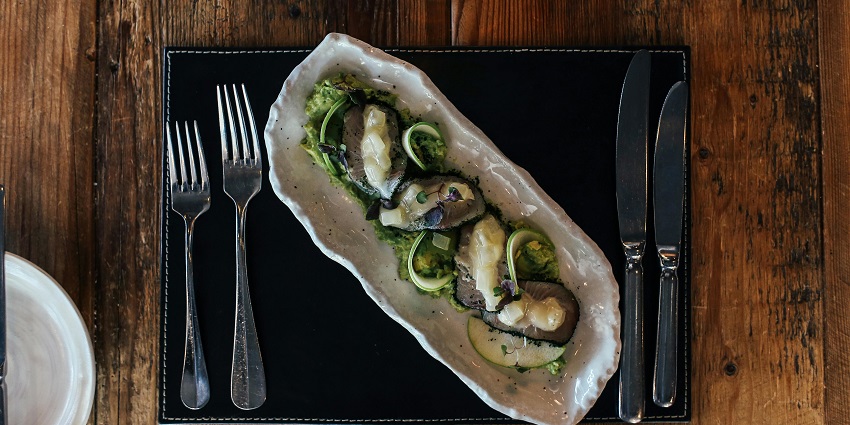 An oyster's dish, the best food in New Zealand, is elegantly sitting on a ceramic plate, garnished with herbs and sauces.