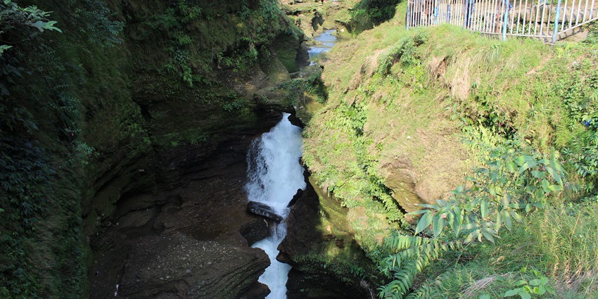 Devi’s waterfall in Pokhara with water flowing on the rocky surface surrounded by greenery