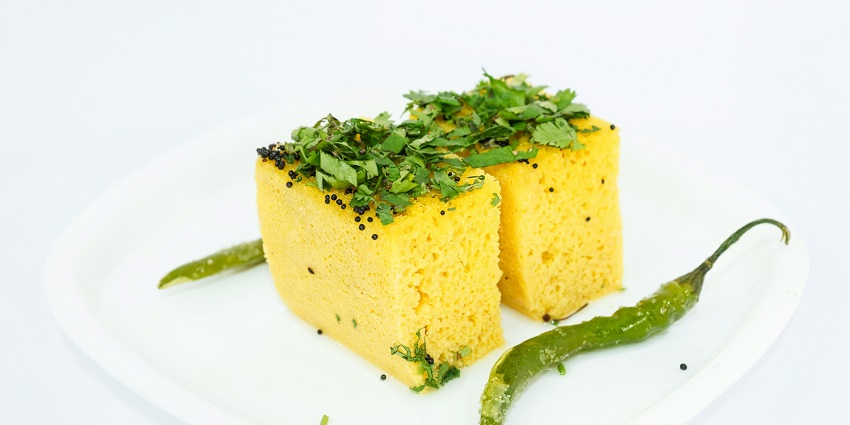 An image showing Gujarati Khaman Dhokla, a steamed, spongy snack garnished with spices.