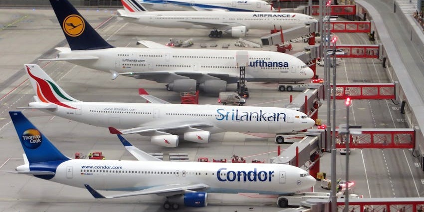 Flights from different airlines are taxied near an airport terminal building with passenger bridges.