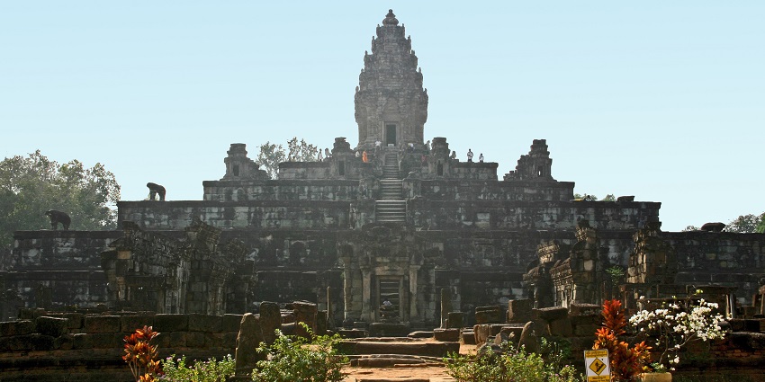 View of the ancient stone temple of Bakong featuring central towers, weathered carvings, and surrounding greenery