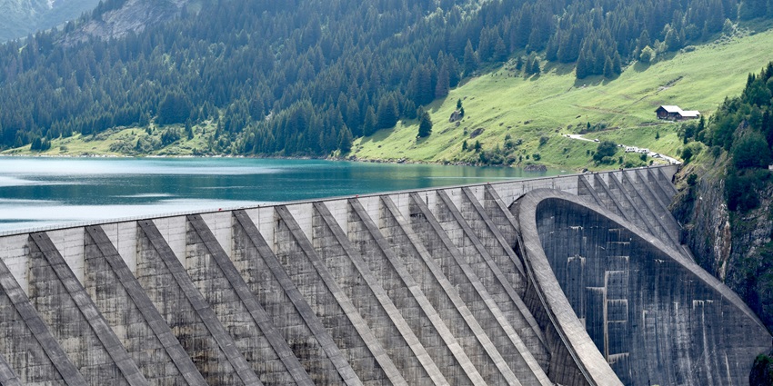 A dam captured during a water release, showcasing its imposing gray concrete structure under a clear sky