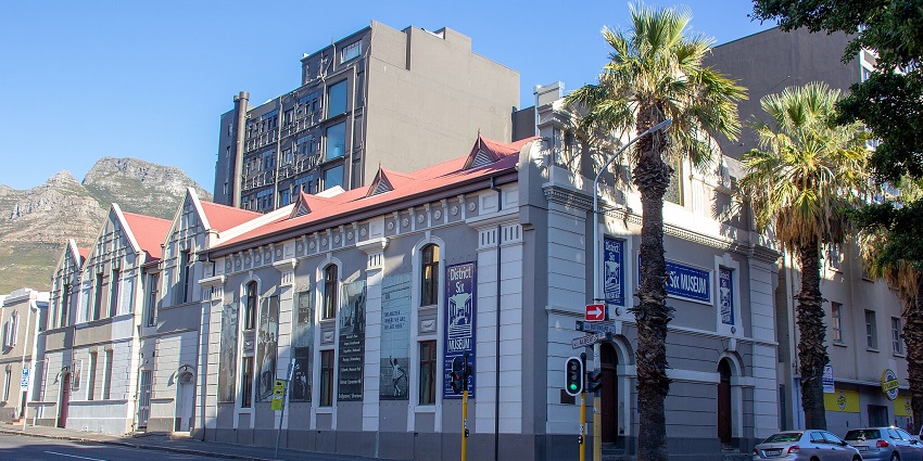 Cape Town's District Six Museum, a red-roofed building with gables, banners, and trees.