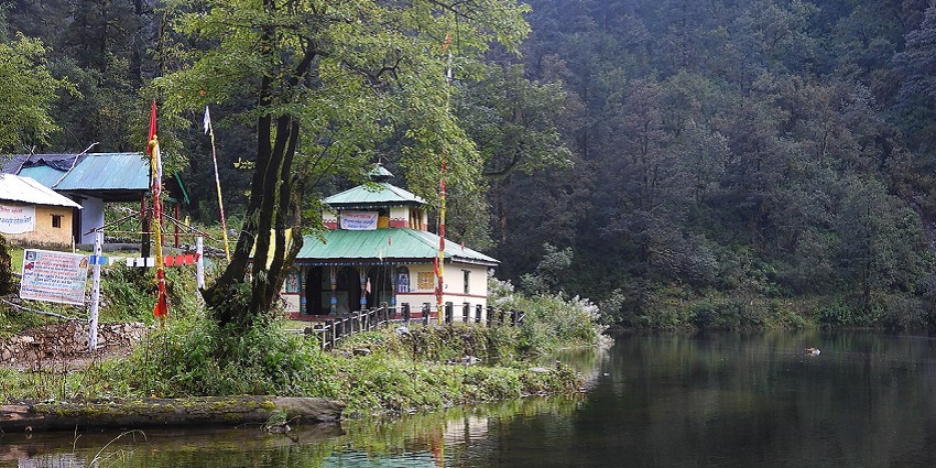 Dodital lake with a large water body surrounded by lush greenery and a temple by the lake