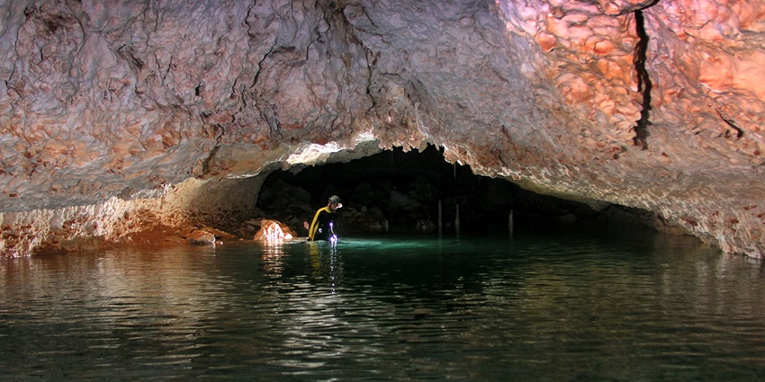 Inside of an underground cave with a person in the underground water wearing safety gear