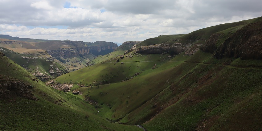 A wide view of the Drakensberg Mountains covered in lush greenery, with rolling clouds.