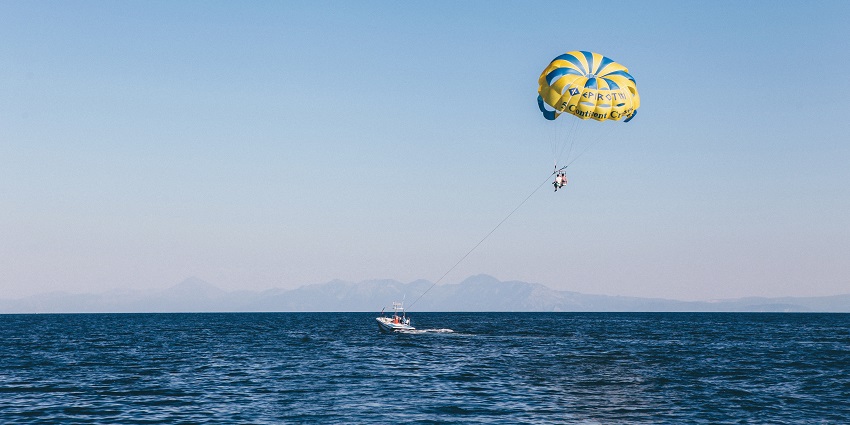 Parasailing over the vast ocean, a colourful parachute lifting two people high in the sky