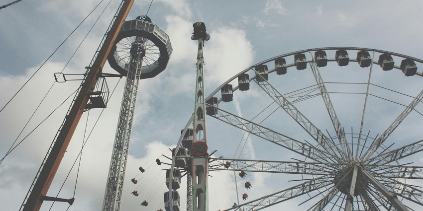 A vibrant theme park scene featuring a carousel and a Ferris wheel, both adorned with lights.