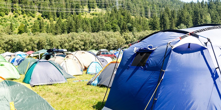 Camp base with multiple different-colour tents amidst forested hills