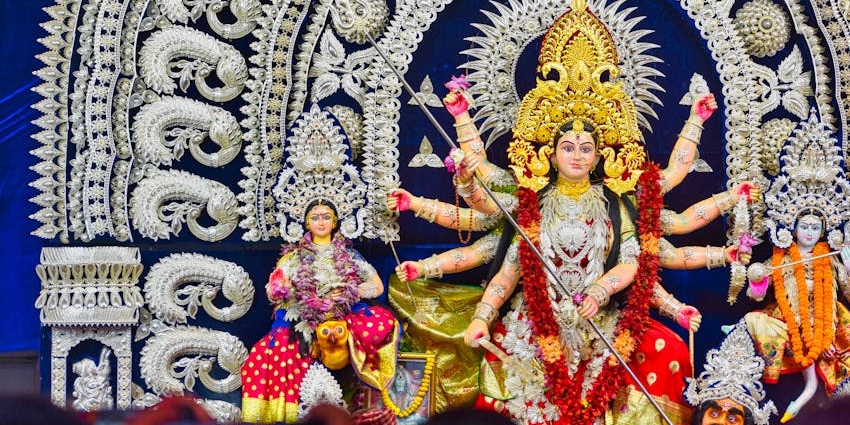 An image of Indian deity, Durga, with multiple arms in colourful attire and an ornate headdress.