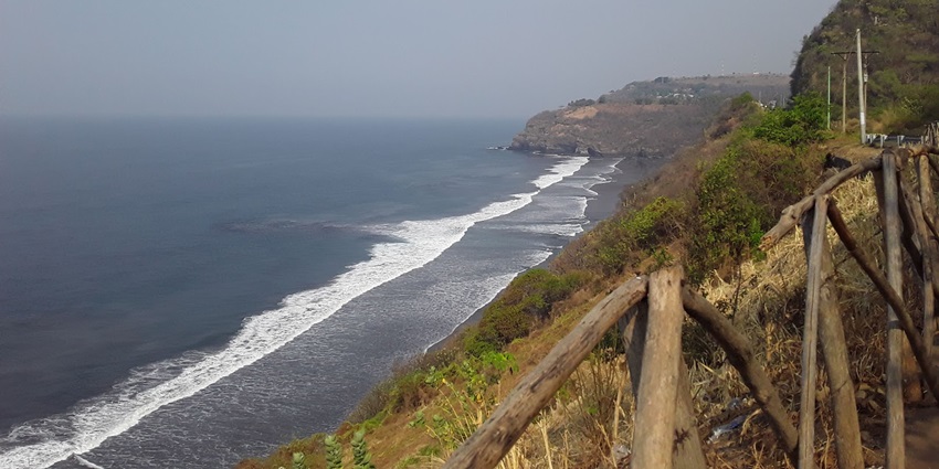 Waves are crashing onto the black sand beach while a rugged coastline is stretching ahead.
