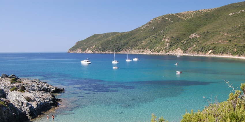 A view of Elba Island with ships sailing and two people enjoying the clear blue water.