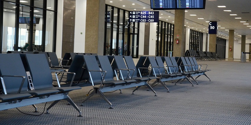 An empty lounge of an airport with chairs lined up in rows and LCD displays of flight info