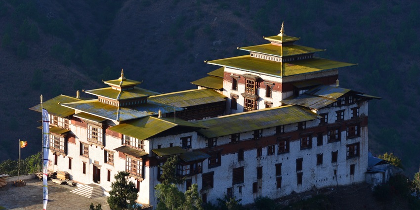An image of a traditional Bhutanese monastery, Trashigang Dzong, with golden roofs, and mountains in the background