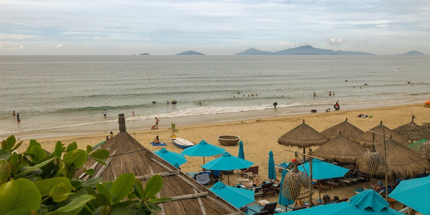Have a romantic beach picnic setup with food and pillows on the sand by the sea.