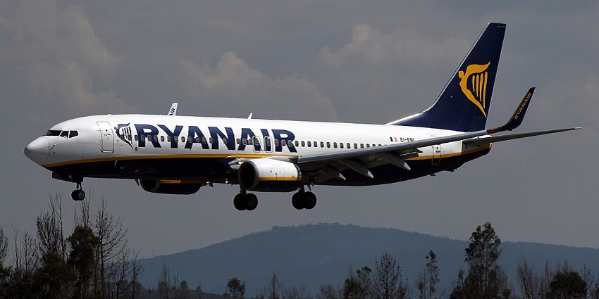 Aeroplane flying through the sky with a scenic mountain landscape in the background.